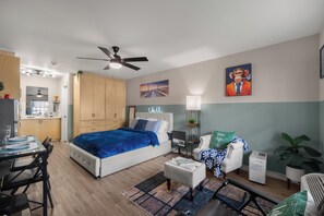 Ein modernes Schlafzimmer mit Bett, Schreibtisch und Stuhl. An der Wand hängt ein Gemälde und es gibt einen Deckenventilator.