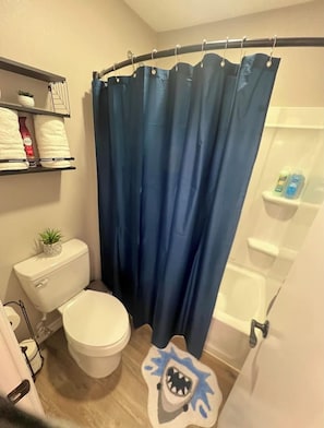 Ein Badezimmer mit einer weißen Toilette, einem blauen Duschvorhang und einem Ablagefach mit Toilettenartikeln.