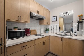 A modern kitchen with wooden cabinets, a stainless steel microwave, a kettle, and a sink. - Brownsville Studio Near SpaceX | Pet-Friendly (Brownsville)