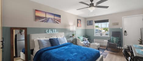 A bedroom with a bed, a desk, a chair, a ceiling fan, and artwork on the walls.