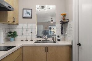 A modern kitchen with white tiles, wooden cabinets, a stainless steel sink, and a ceiling fan. - Brownsville Studio Near SpaceX | Pet-Friendly (Brownsville)