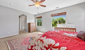 A bedroom with a large bed, a ceiling fan, a window with a view of greenery, and a door leading to another room. - 5BR Fallbrook Hideaway | Hot Tub + Scenic Getaways (Fallbrook)