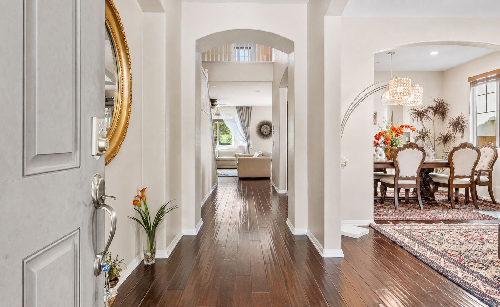 A hallway with a wooden floor, a dining area with a patterned rug, and a large mirror on the left.