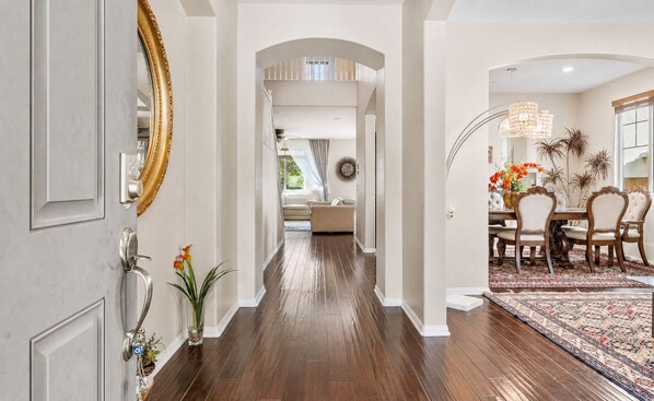 A hallway with a wooden floor, a dining area with a patterned rug, and a large mirror on the left. - 5BR Fallbrook Hideaway | Hot Tub + Scenic Getaways (Fallbrook)