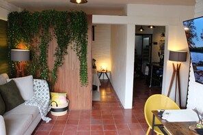 En moderne stue med sofa, spisebord og en gul stol. Der er en væg med grønne planter og en lampe.