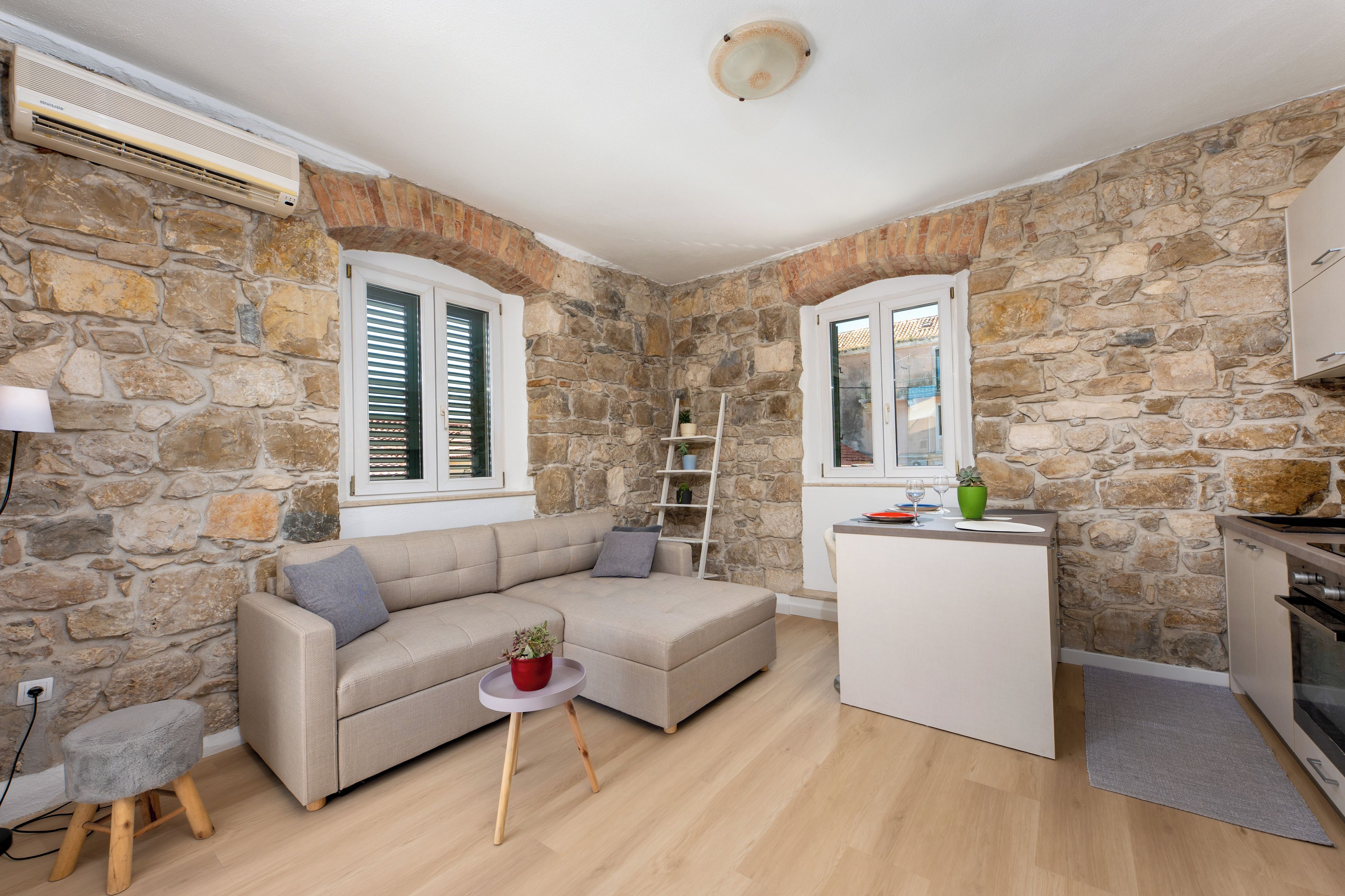 A cozy living area with a stone wall, a sofa, a small table with a plant, and a kitchenette.