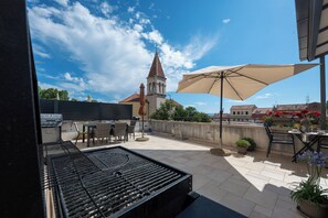 Eine Terrassensitzgruppe im Freien mit Grill, Stühlen und einem großen Sonnenschirm.