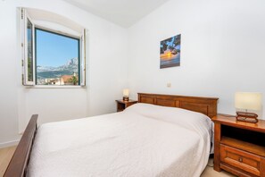 Ein Schlafzimmer mit einem Bett, einem Nachttisch, einer Lampe, einem Gemälde und einem Fenster mit Blick auf einen Berg und eine Stadt.
