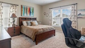 Een slaapkamer met een bed, een bureau, een stoel, een plafondventilator en een raam met gordijnen.
