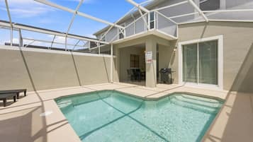 A swimming pool with a covered patio area, a table, and chairs.
