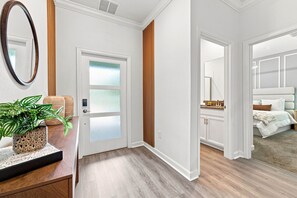 Un pasillo que conduce a un dormitorio con una cama, un baño con un lavamanos y una puerta con paneles de vidrio esmerilado.