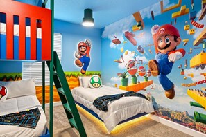 Un dormitorio con cama, almohadas, una escalera verde y un mural con Mario y Luigi.