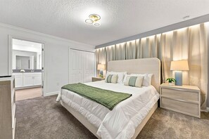 A modern bedroom with a large bed, bedside lamps, a nightstand, and a view of the bathroom.