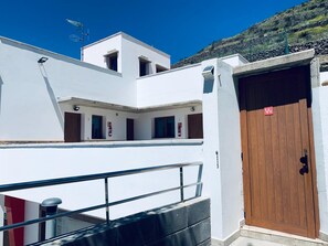 A white building with a brown door, a balcony, and a clear blue sky. - Cave Apartment With Terrace (Artenara)