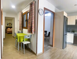 A modern kitchen with a refrigerator, sink, and dining area with chairs and a table. - Cave Apartment With Terrace (Artenara)