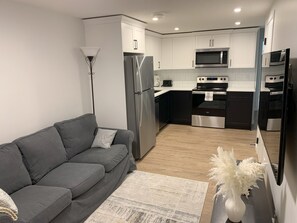 Eine moderne Küche mit einem grauen Sofa, einer weißen Vase mit weißen Blumen und einem Holzboden.