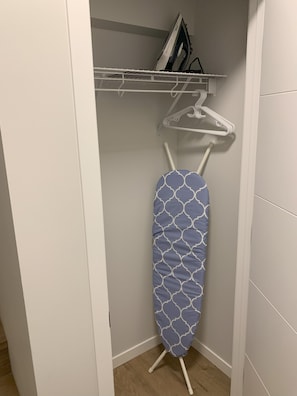 Ein Kleiderschrank mit Kleiderstange, Bügelbrett und einem Bücherregal.