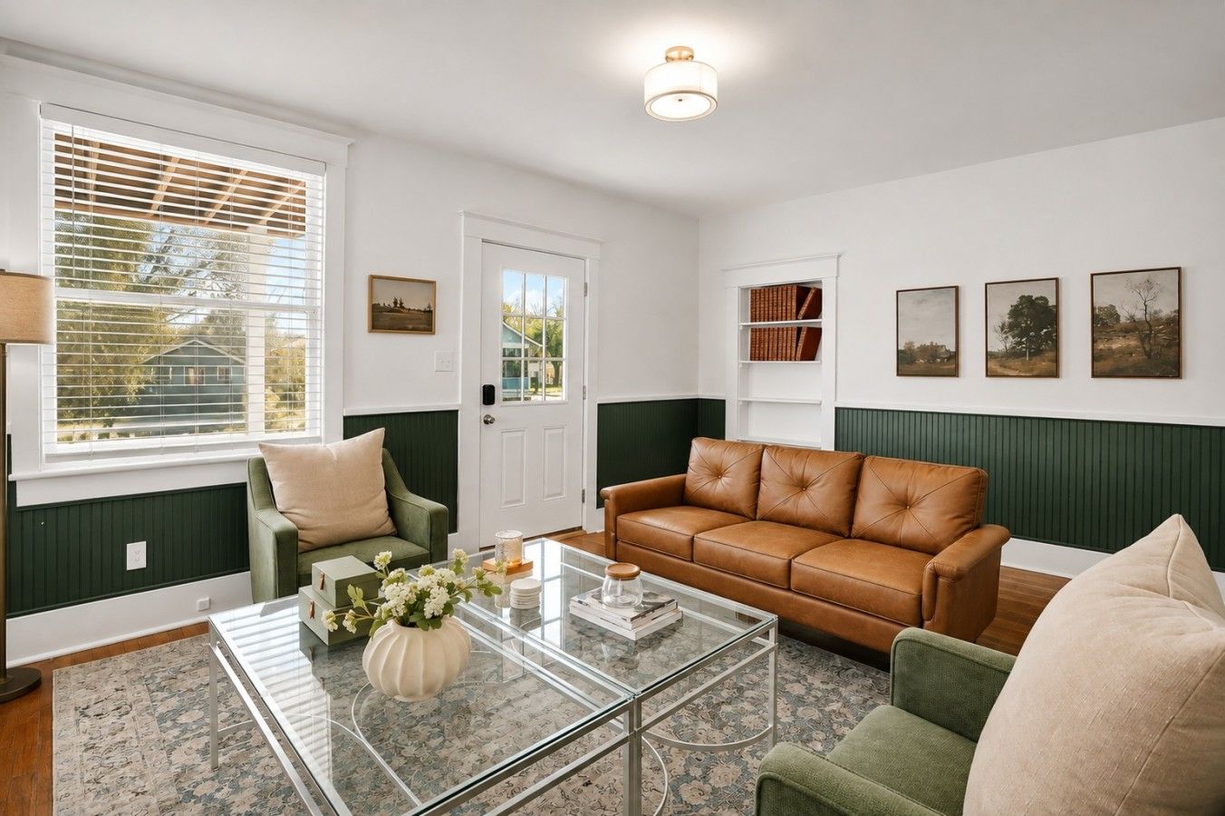 A living room with a green and white color scheme, featuring a leather sofa, a glass coffee table, and a green armchair.