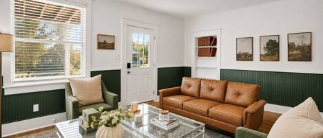 A living room with a green and white color scheme, featuring a leather sofa, a glass coffee table, and a green armchair.