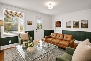 A living room with a green and white color scheme, featuring a leather sofa, a glass coffee table, and a green armchair. - Charming & Modern Savannah Retreat | Steps to Daffin Park (Savannah)