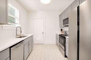 A modern kitchen with stainless steel appliances, a white countertop, and a patterned floor. - Charming & Modern Savannah Retreat | Steps to Daffin Park (Savannah)