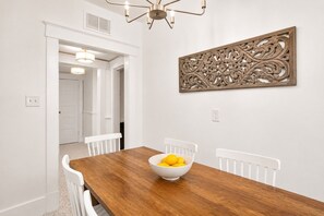 A dining area with a wooden table, white chairs, and a decorative wall piece. - Charming & Modern Savannah Retreat | Steps to Daffin Park (Savannah)