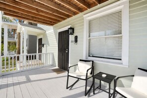 A covered porch with a white railing, a door, and two chairs with a small table. - Charming & Modern Savannah Retreat | Steps to Daffin Park (Savannah)