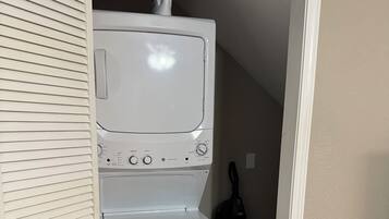 A laundry room with a stacked washer and dryer, a bottle of detergent, and a vacuum cleaner.