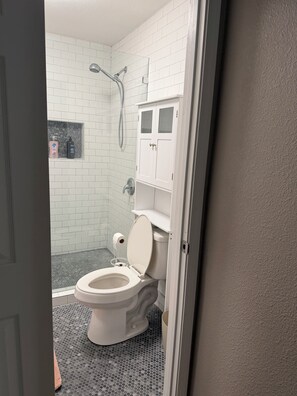 Un baño con inodoro, ducha y un pequeño estante con artículos de aseo.