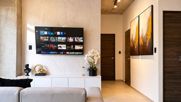 A modern living room with a flat-screen TV mounted on the wall, a white console table, and a large abstract painting. - Park Tower | Santa Elena Sur Area & U.S. Embassy (Nuevo Cuscatlan)
