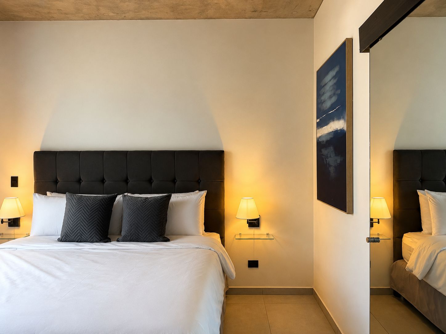 Ein Hotelzimmer mit einem großen Bett, zwei Nachttischlampen, einem Wandbild und einem Spiegel.