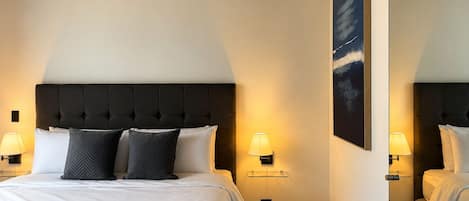 Ein Hotelzimmer mit einem großen Bett, zwei Nachttischlampen, einem Wandbild und einem Spiegel.