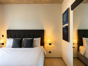 Et hotelværelse med en stor seng, to sengeborde med lamper, et billede på væggen og et spejl.