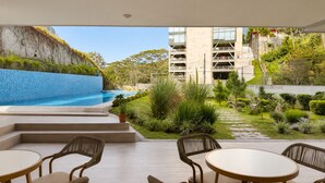A pool area with a view of a building and a garden. - Park Tower | Santa Elena Sur Area & U.S. Embassy (Nuevo Cuscatlan)
