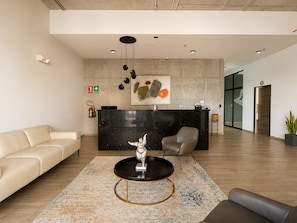 Et moderne receptionsområde med en sort skranke, en beige sofa, en grå lænestol og en unik skulptur på et sofabord.