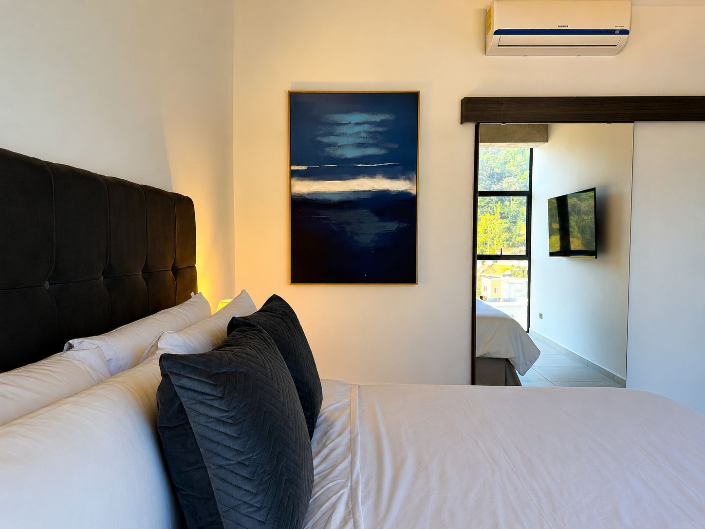 Ein Schlafzimmer mit einem großen Bett, einer Wandklimaanlage, einem Gemälde und einem Fenster mit Blick ins Freie.