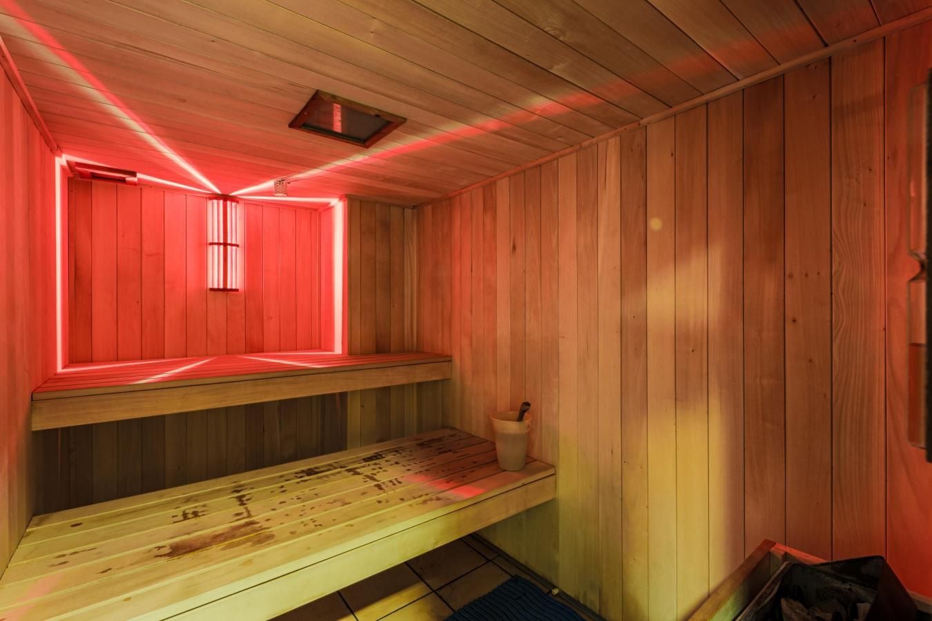 Un sauna avec des bancs en bois et une lumière rouge.