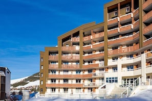 A multi-story hotel with balconies, a ski slope in the background, and a clear blue sky. - Wifi, 100m from ski slopes, swimming pool, sauna, balcony, ski locker, 19m², Alpe d'Huez (L'Alpe d'Huez)