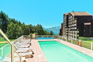 A swimming pool with lounge chairs, a clear view of mountains, and a building with balconies. - Wifi, 100m from ski slopes, swimming pool, sauna, balcony, ski locker, 19m², Alpe d'Huez (L'Alpe d'Huez)
