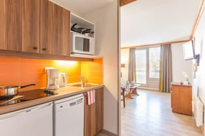 A compact kitchen with a microwave, stove, and dishwasher. A dining area with a table and chairs is visible through an open doorway. - Wifi, 100m from ski slopes, swimming pool, sauna, balcony, ski locker, 19m², Alpe d'Huez (L'Alpe d'Huez)