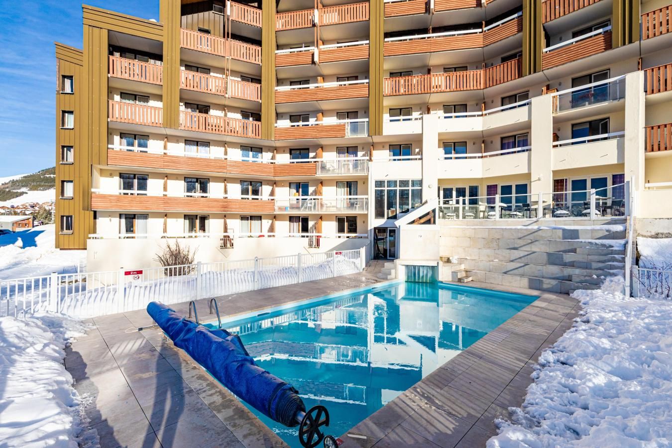 Un hôtel à plusieurs étages doté d’une piscine, d’un espace extérieur aménagé et surplombant un paysage enneigé.