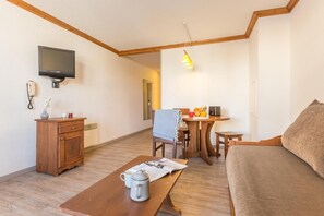 A cozy room with a wooden table, a sofa, a TV mounted on the wall, and a small dining area. - Wifi, 100m from ski slopes, swimming pool, sauna, balcony, ski locker, 19m², Alpe d'Huez (L'Alpe d'Huez)