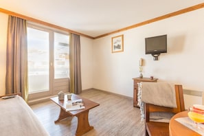 A hotel room with a bed, a small table with a newspaper, a chair, a television mounted on the wall, and a window with curtains. - Wifi, 100m from ski slopes, swimming pool, sauna, balcony, ski locker, 19m², Alpe d'Huez (L'Alpe d'Huez)