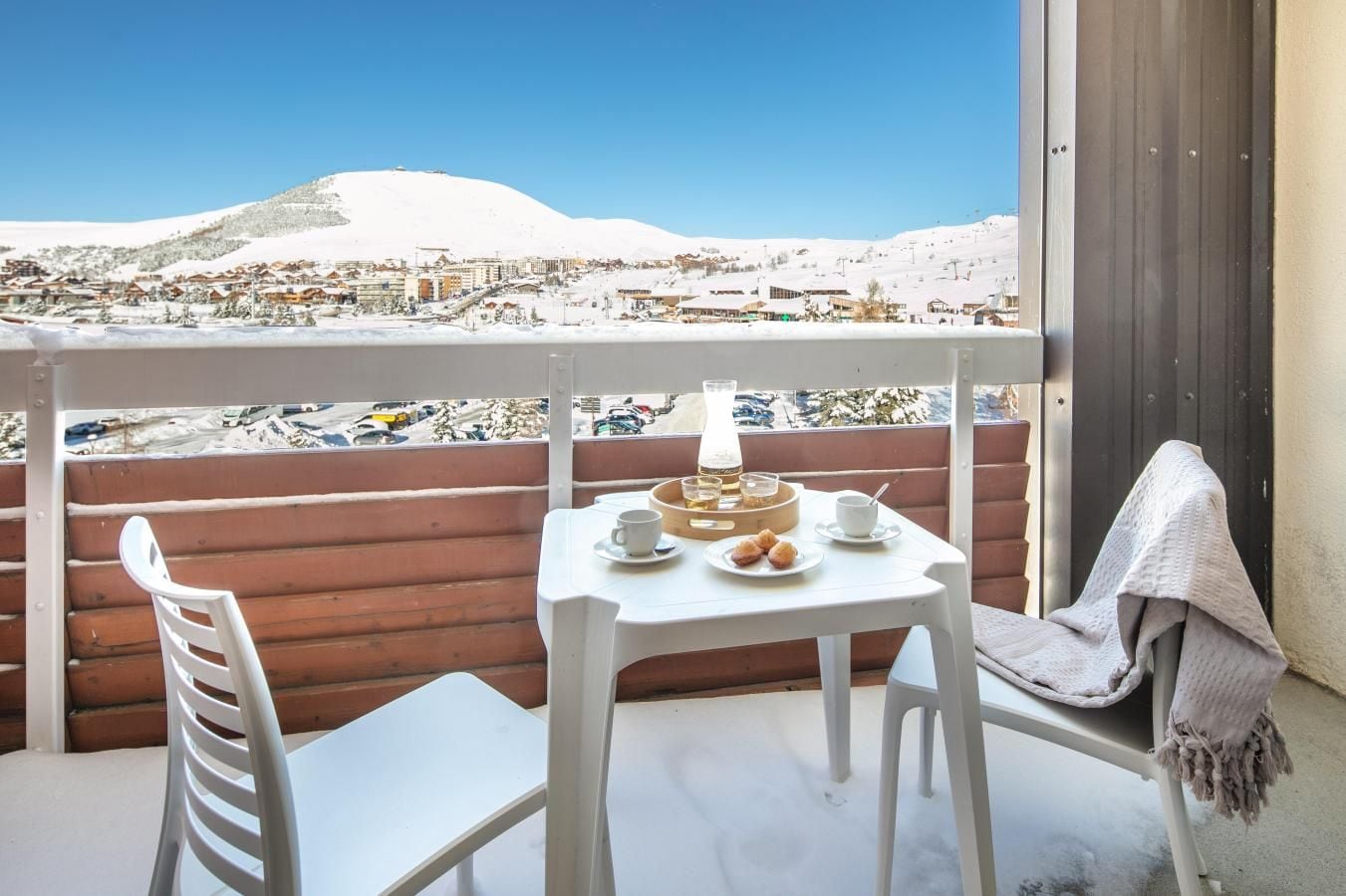 Un balcon avec une table dressée pour deux personnes, donnant sur un paysage enneigé avec des bâtiments et une colline.
