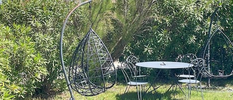 A metal outdoor seating area with a round table and chairs, surrounded by greenery and trees.
