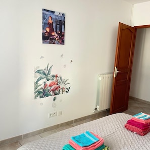 Een kamer met een bed, een radiator, een houten deur en decoraties aan de muur, waaronder een Boeddha en een tropische afbeelding.