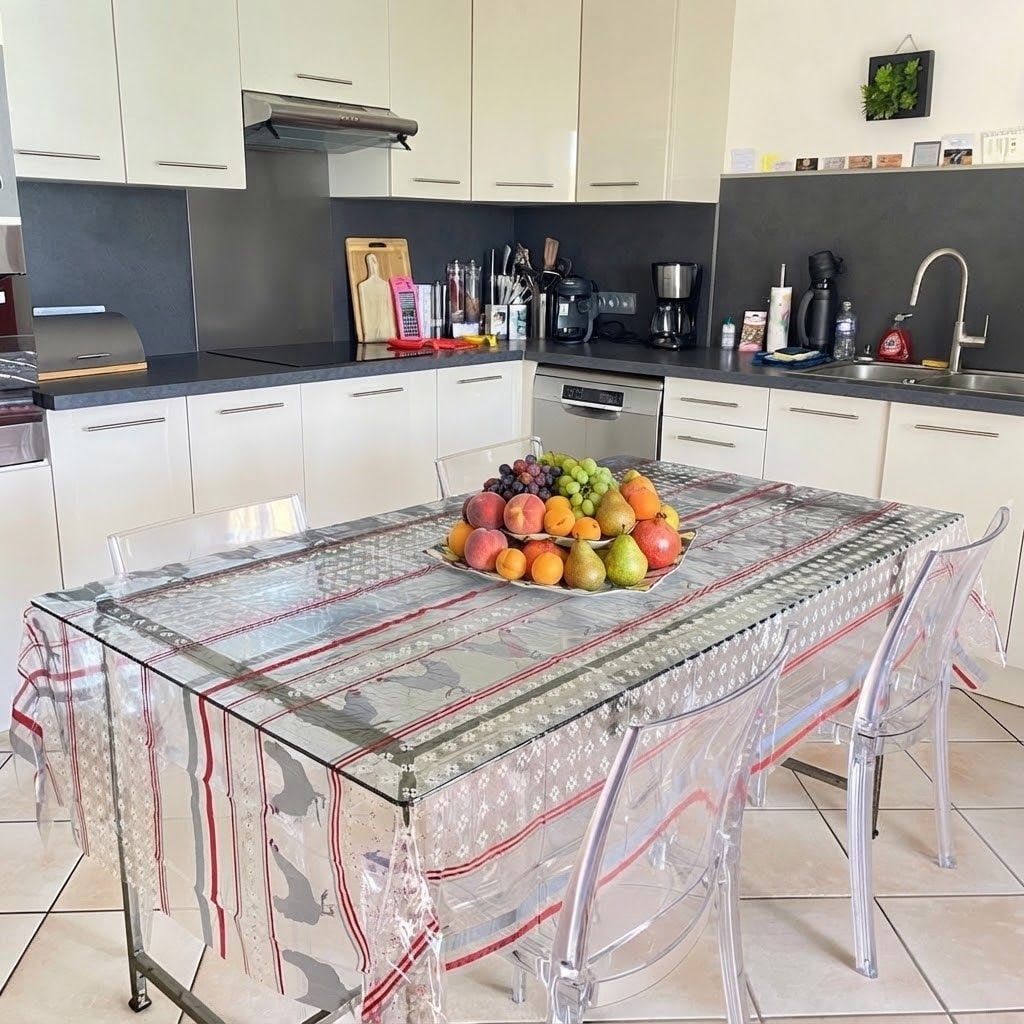 Une cuisine moderne avec des armoires blanches, une hotte de cuisinière en acier inoxydable et une table en verre agrémentée d’un centre de table composé de fruits.