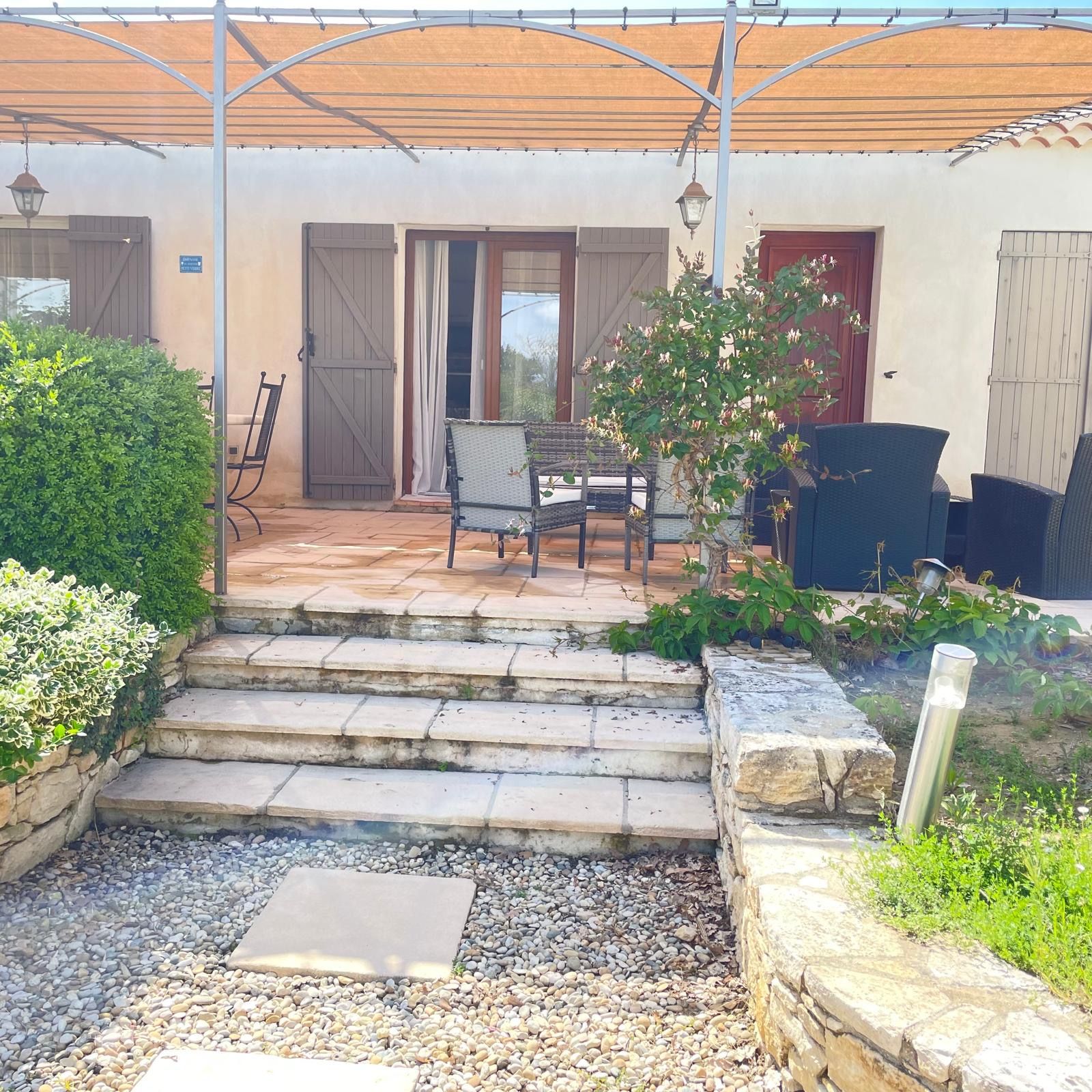 A covered patio with a stone staircase leading to a seating area with chairs and a table.