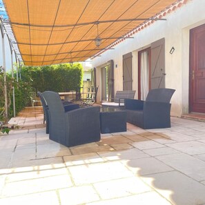 An outdoor patio with wicker furniture, a covered area, and a view of the building's exterior. - Caro's Villa in Blauzac (Blauzac)