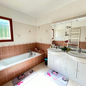 A bathroom with a bathtub, two sinks, a mirror, and a window. - Caro's Villa in Blauzac (Blauzac)